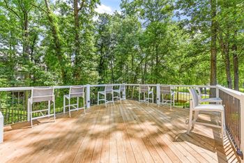 A wooden deck with white chairs and a railing overlooking a forest. at Southpark Commons Apartment Homes, North Carolina, 28210
